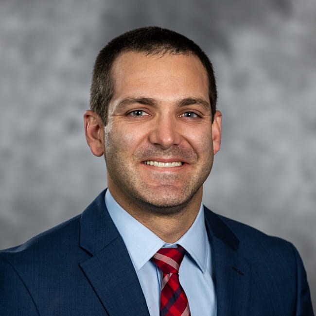 Kyle Andrews, MD, in a navy suit and red plaid tie